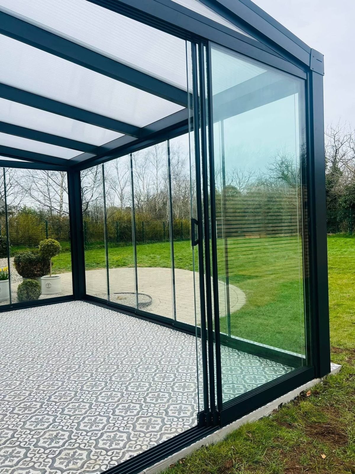 Frameless sliding glass panels stacked to one side under a polycarbonate roof