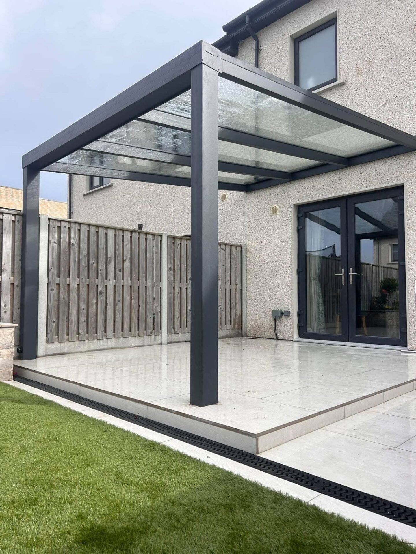 Open aluminium pergola with a clear glass roof over a patio at the back of a house