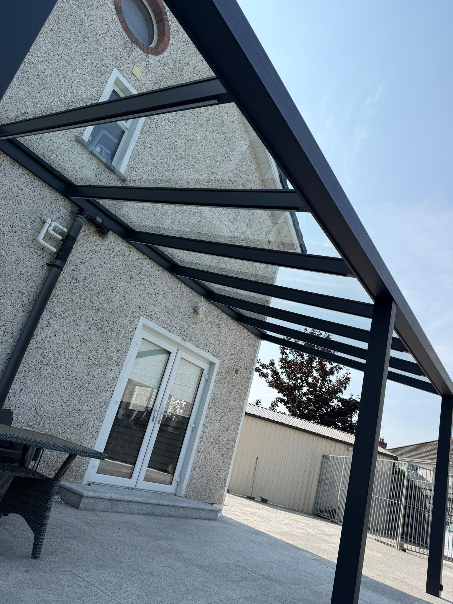 Aluminium pergola veranda with a clear glass roof against a pebble dash house