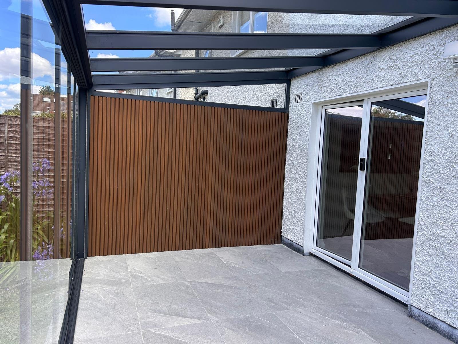 Pergola veranda side enclosure with a composite cladding wall and frameless sliding glass